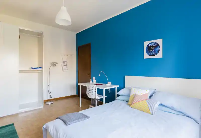 Chambre lumineuse et soignée avec un lit double devant un mur bleu vif, coussins décoratifs et un petit bureau — idéale pour un séjour confortable.