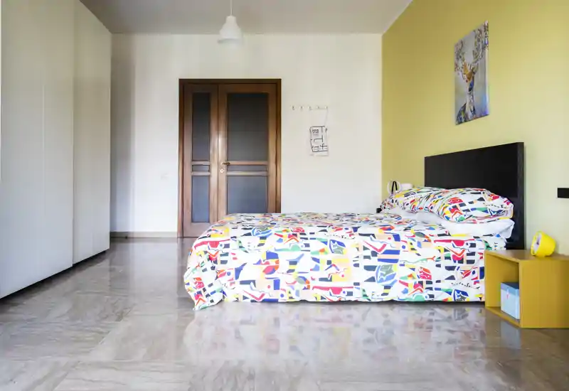 Camera da letto moderna e luminosa con letto matrimoniale colorato, arredi minimal e pavimento in piastrelle lucide — perfetta per annunci.