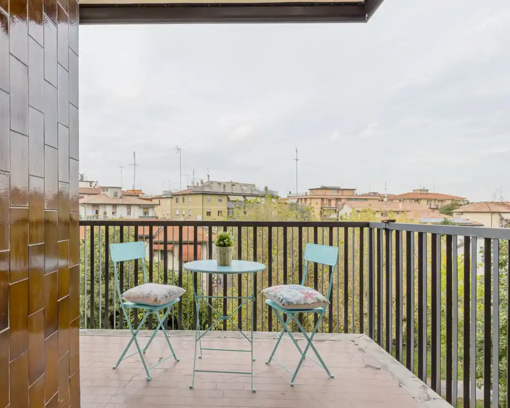 Balcone arioso con tavolino da bistrò, due sedie pieghevoli turchesi e una piantina in vaso — perfetto per un caffè mattutino con vista sulla città.