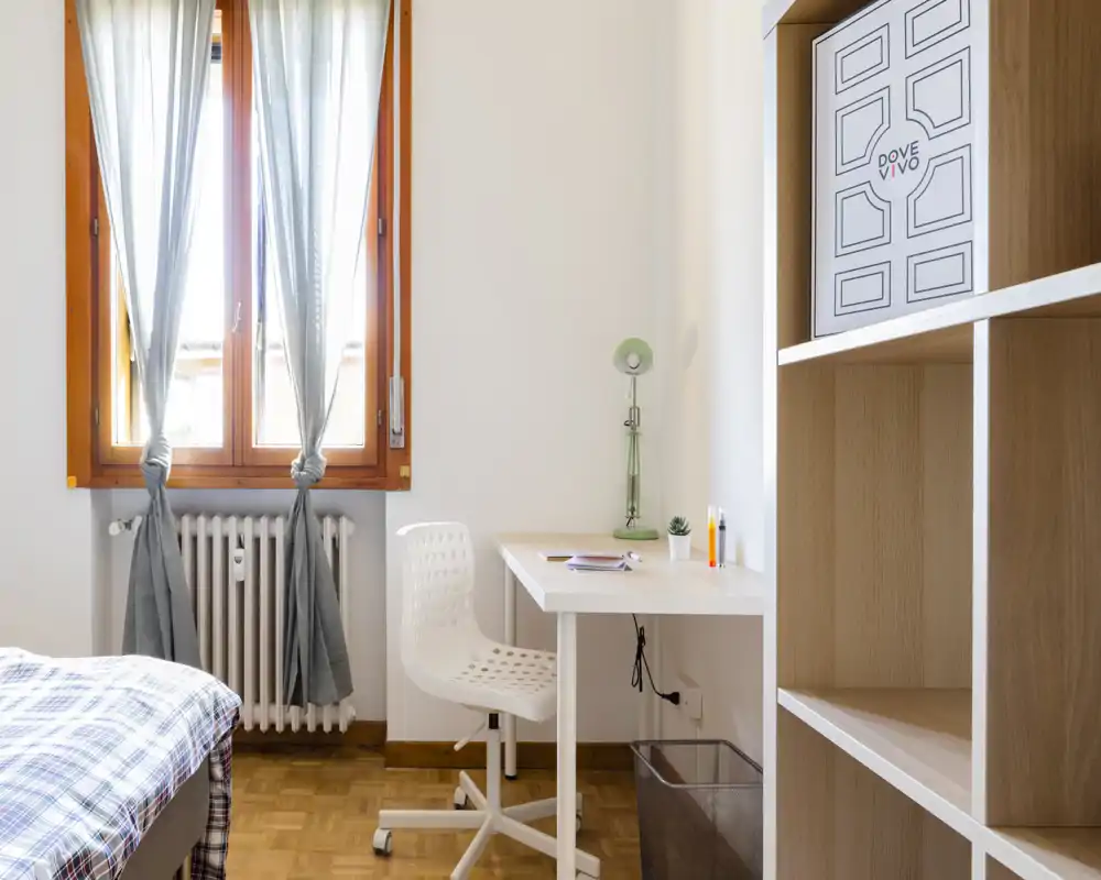 Rincón de dormitorio luminoso y ordenado con cama individual, escritorio y estantería. La luz natural de la ventana aporta una atmósfera limpia y acogedora, ideal para estudiar o descansar.