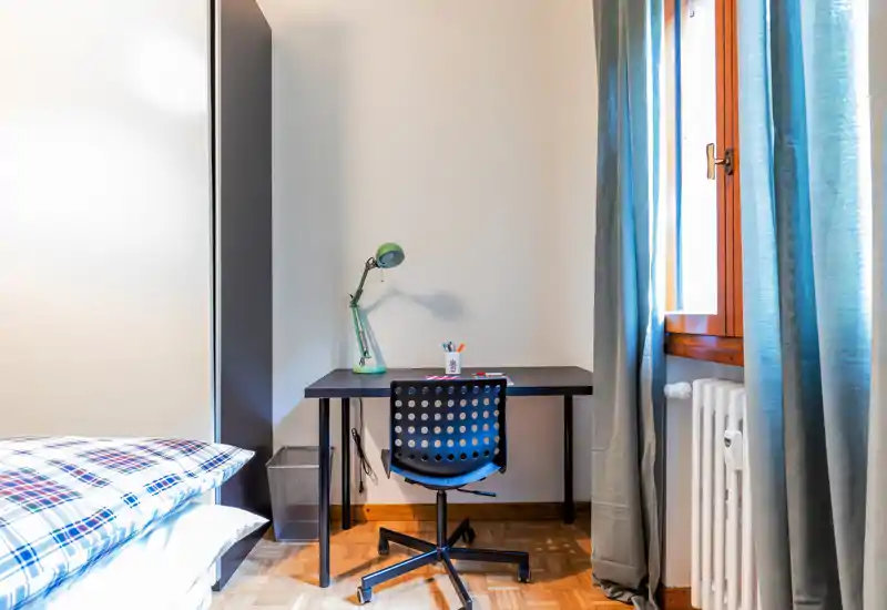 Angolo camera luminoso e ordinato con letto singolo, scrivania e sedia girevole vicino alla finestra con luce naturale.