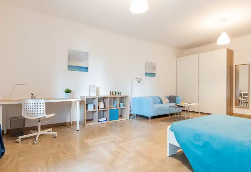 Camera da letto luminosa e moderna con letto matrimoniale in lenzuola blu, divano azzurro, scrivania e guardaroba — ariosa e arredata con gusto per affitti brevi.