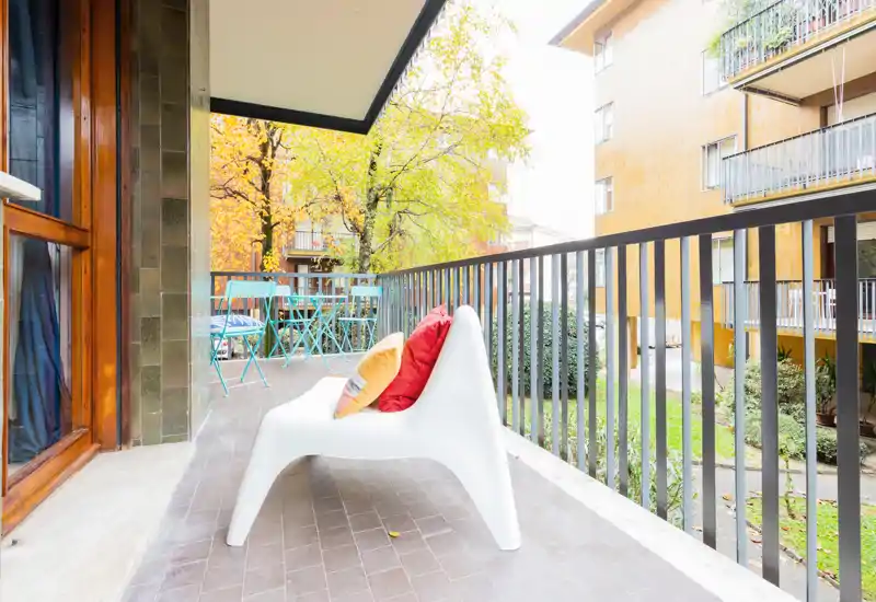 Balcone soleggiato con poltrona moderna e cuscini colorati, più un piccolo set da bistro — ideale per caffè mattutino e relax all'aperto.