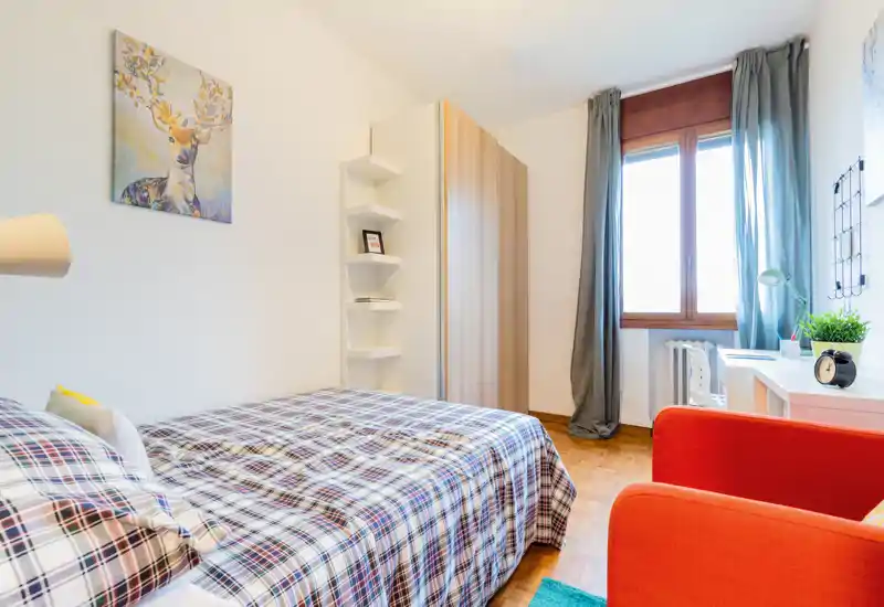 Sunny, well-styled bedroom with a plaid-covered double bed, a wardrobe, desk by the window and warm parquet flooring.