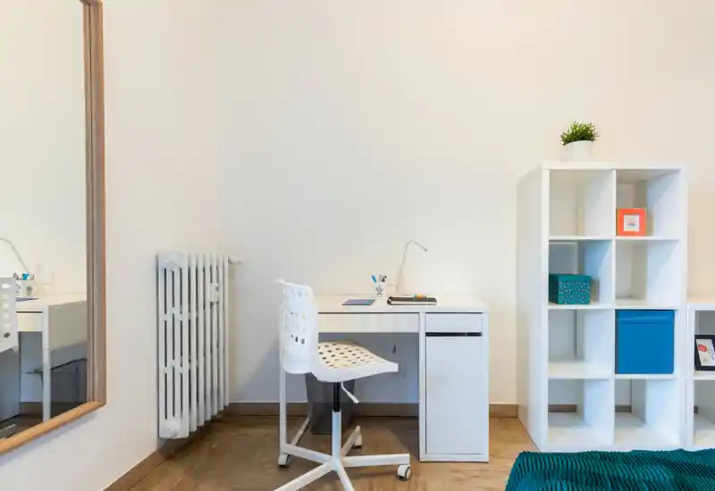 Angolo studio luminoso e minimal con scrivania bianca, sedia traforata e libreria a cubi. L’allestimento ordinato e la piantina danno un tocco funzionale perfetto per lavorare da casa.