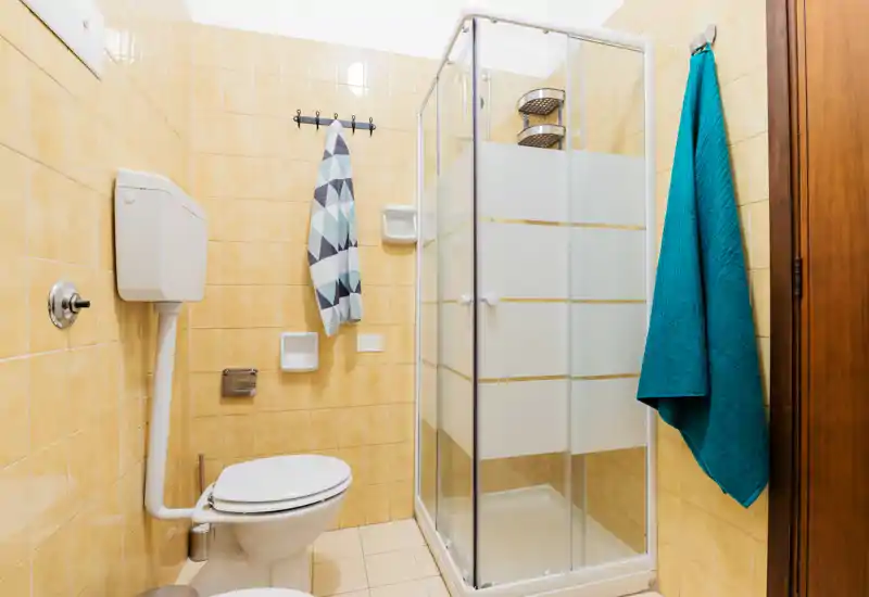 Clean, compact bathroom with a shower cubicle, toilet with high cistern and tiled walls in warm tones. Bright, well-lit space suitable for a short-term rental.