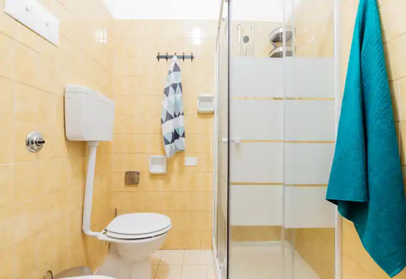 Compact, clean bathroom with a tiled interior, toilet and a glass-enclosed shower. Bright, simple design with colorful towels adding contrast.