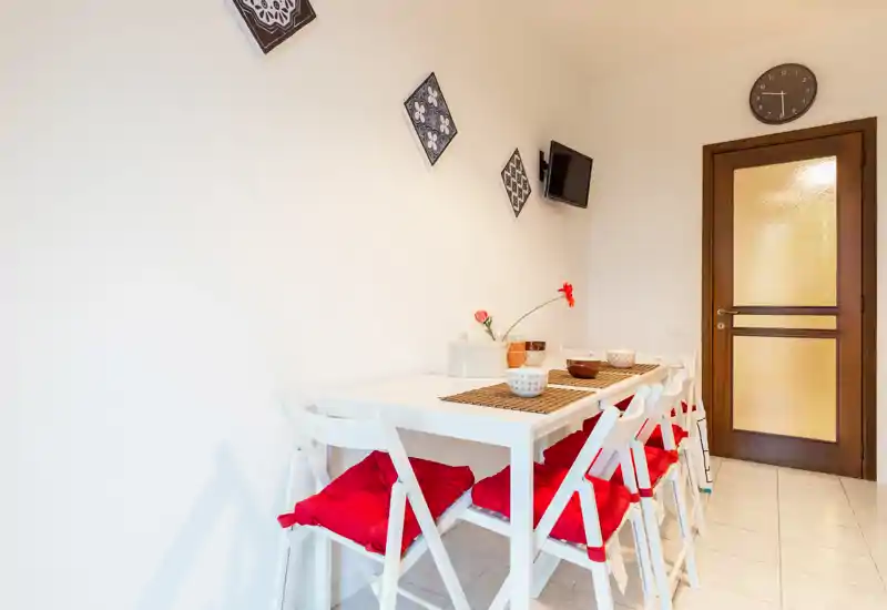 Bright, modern dining corner with a white table and matching folding chairs accented by red seat cushions, simple tableware and wall decor — perfect for casual meals.