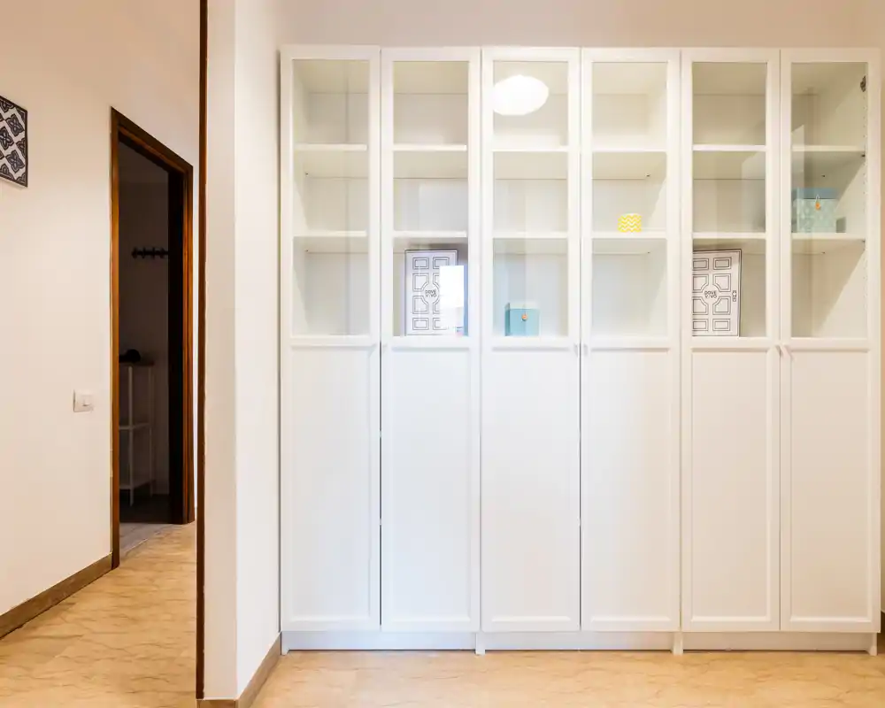 Ingresso/corridoio luminoso con alti armadi bianchi e una porta che conduce all'interno. Pavimento e pareti neutre che donano una prima impressione ordinata.