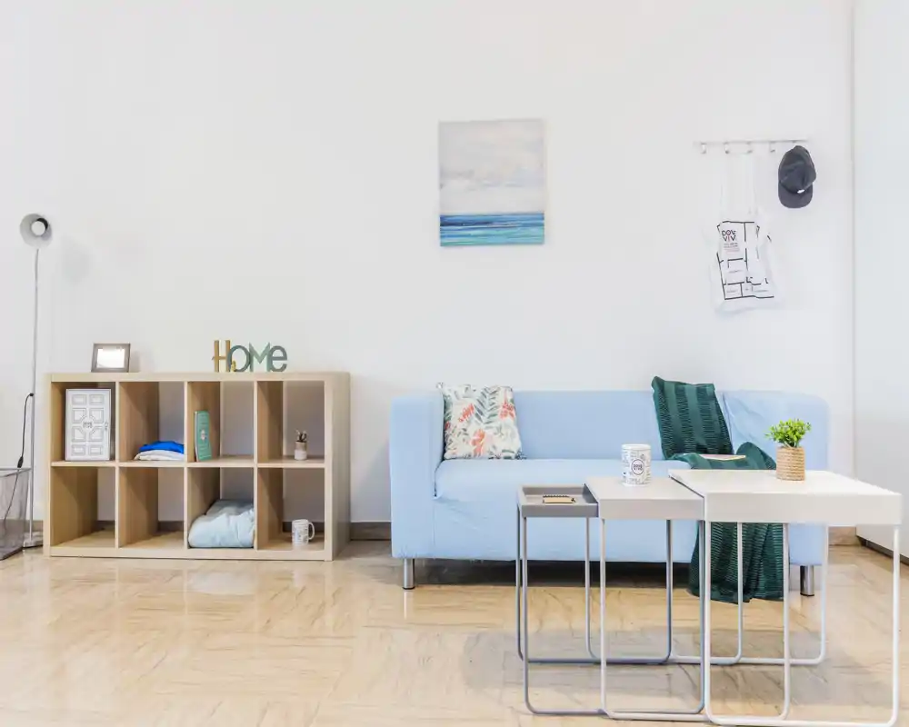 Bright, modern living room with a light-blue sofa, decorative cushions and nested coffee tables, styled with minimal shelving and a small plant for a fresh, airy feel.