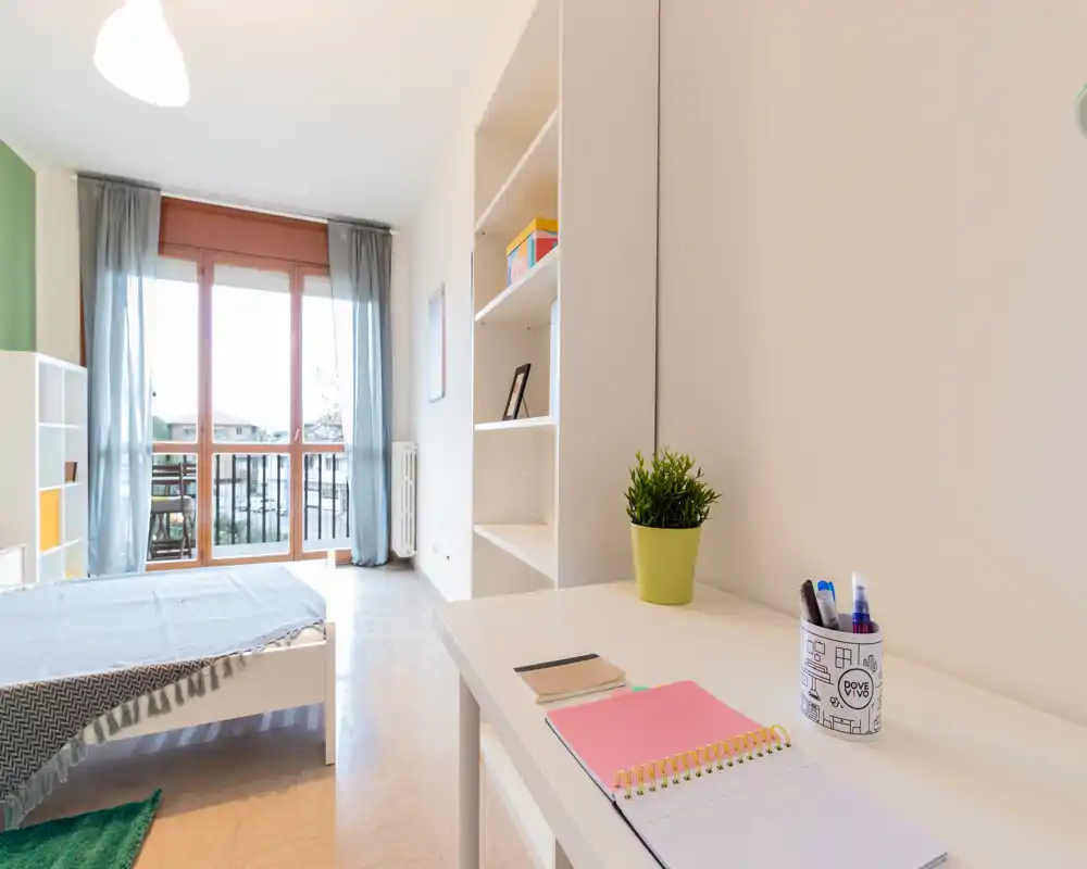 Bright, modern bedroom with a single bed, desk and shelving by large balcony doors bringing abundant natural light—ideal for students or short-term rentals.