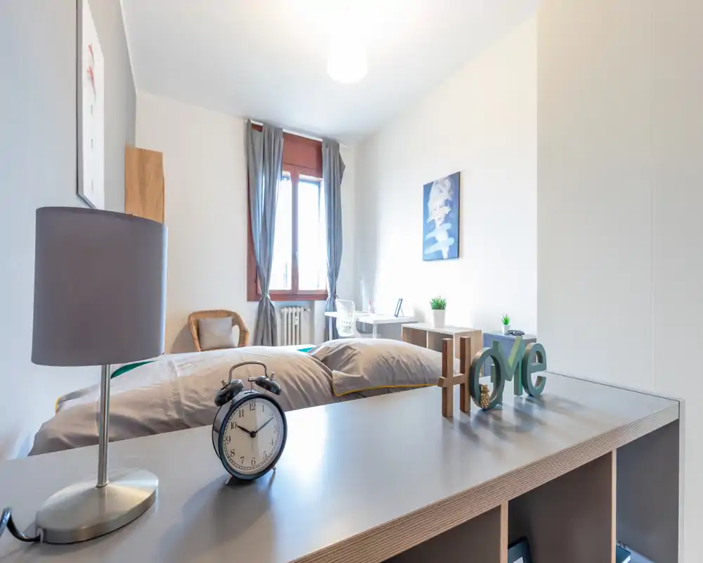 Bright, well-staged bedroom with a neatly made bed, bedside lamp and decorative accents. Natural light from the window and neutral tones create a calm, welcoming atmosphere ideal for rental listings.