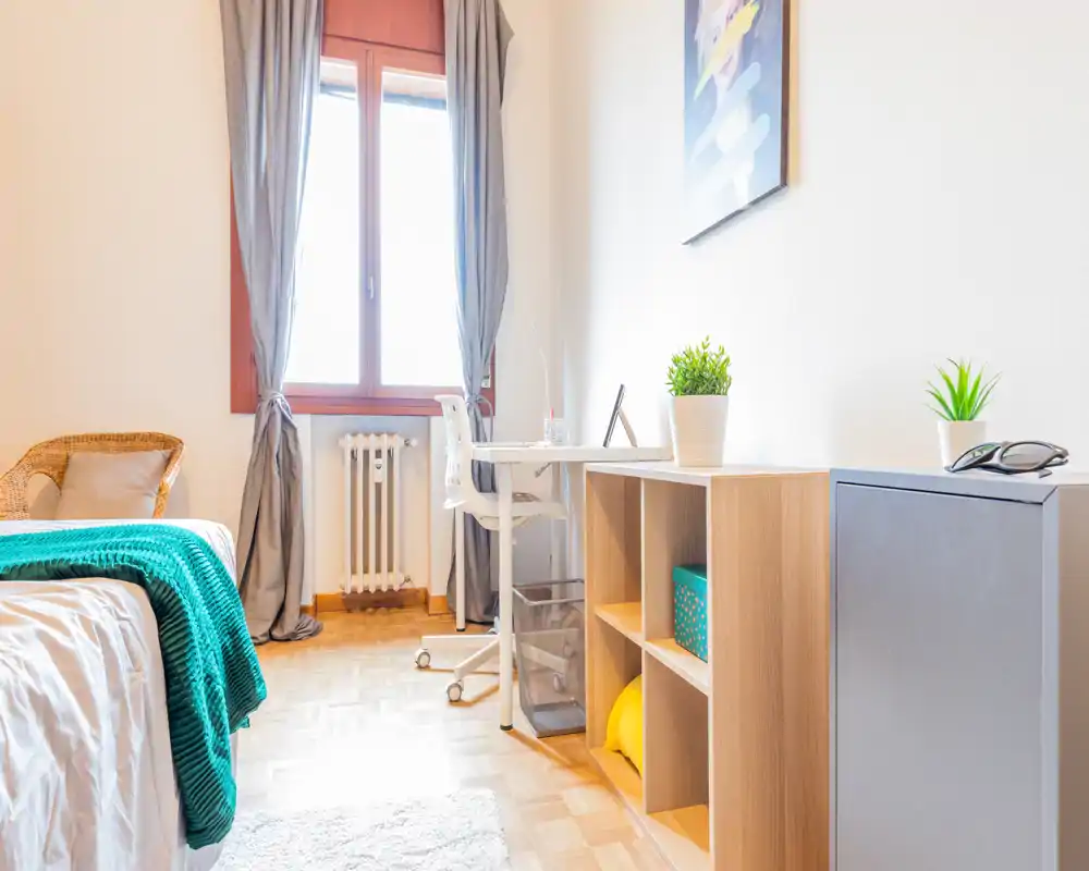 Bright, cozy bedroom corner with a neatly made bed, textured throw and a small desk by the window — ideal for a comfortable stay or remote work.