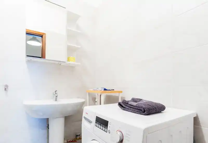 Bright, compact bathroom with a pedestal sink, mirror cabinet and a front-loading washing machine neatly placed under a folded towel.