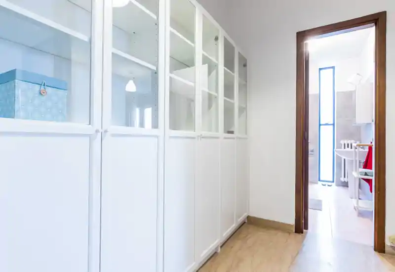 Bright entry/corridor with built-in white cabinets and a view into a bathroom; clean, minimal and practical space ideal for storage.