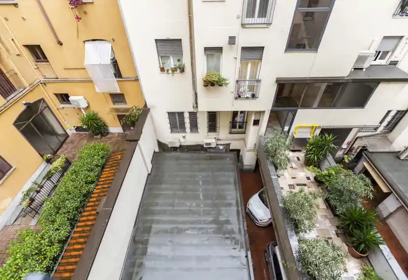 Bright inner courtyard/terrace view with planted borders and potted shrubs beside parked cars; clean, well-maintained exterior space suitable for a city apartment.