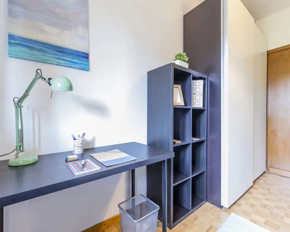 Angolo studio luminoso e minimal con scrivania scura, lampada verde regolabile, libreria a cubi e quadro decorativo — perfetto per il lavoro concentrato.