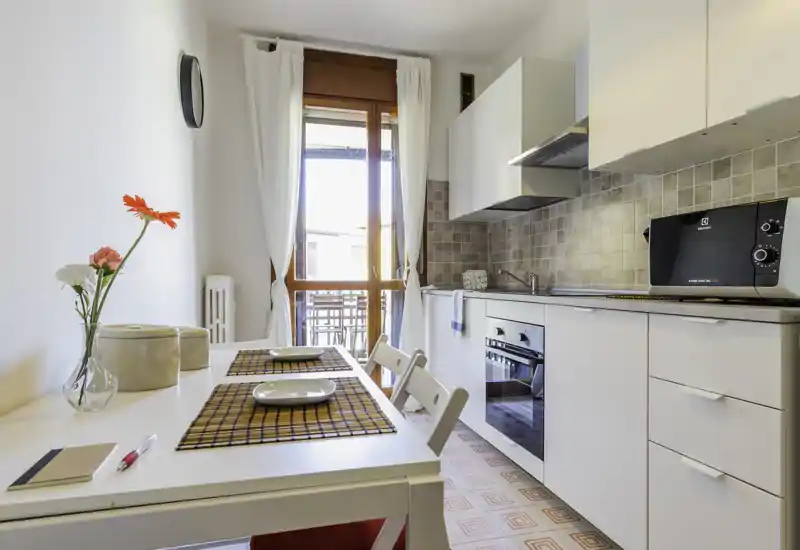 Bright modern kitchen with integrated oven, microwave and a small dining table set for two; natural light from a balcony door creates a fresh, welcoming atmosphere.