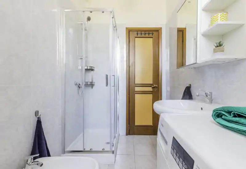 Bright, clean bathroom with a glass shower enclosure, sink, mirrored cabinet and washing machine visible on the countertop.