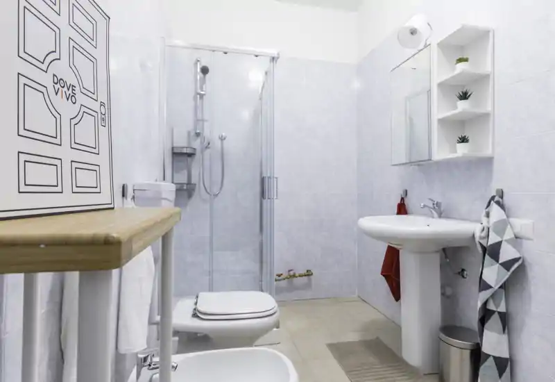 Clean, modern bathroom with a glass-enclosed shower, pedestal sink, toilet and bidet; light tiles and minimal decor create a fresh, tidy space.
