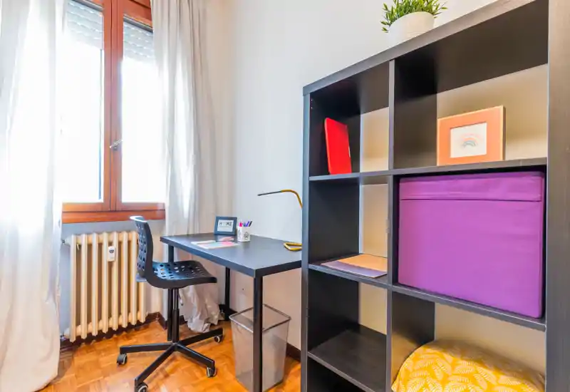 Bright, tidy bedroom workspace with a desk by the window and organized shelving; clean lines and colourful storage create a welcoming, functional corner for remote work.