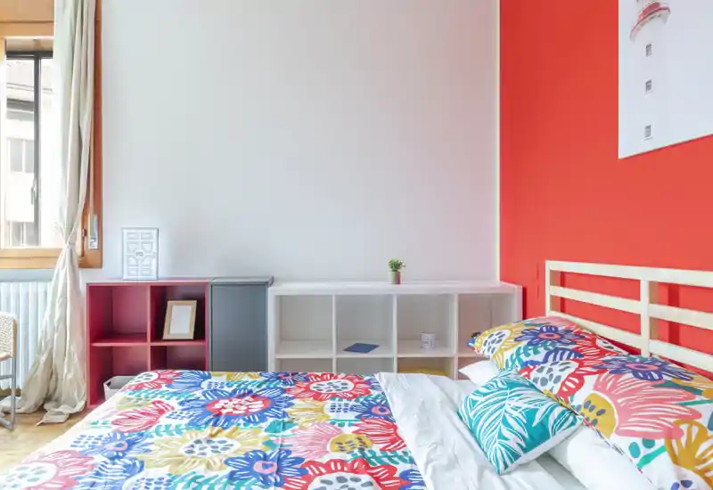 Bright, colorful bedroom with a queen-size bed, patterned bedding and a simple wooden headboard; natural light streams from the window making the space cheerful.