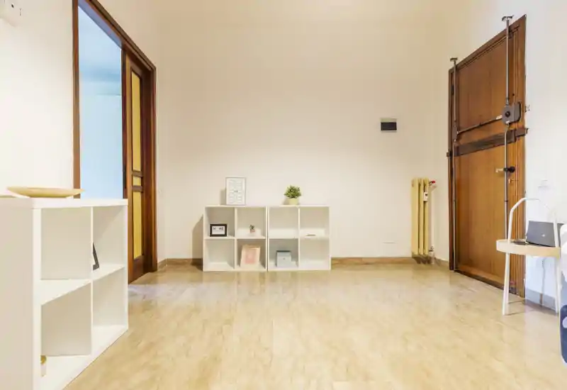 Minimal, tidy entryway with a wooden entrance door, tiled floor and low shelving; bright neutral walls and modest decorative items create a clean, welcoming arrival space.