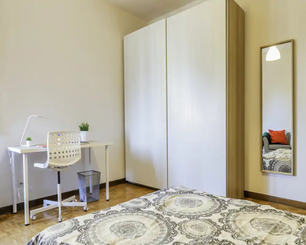 Dormitorio luminoso y bien decorado con ropa de cama estampada, un gran armario blanco, un escritorio pequeño y silla; ideal para una persona que busca un espacio moderno y ordenado.
