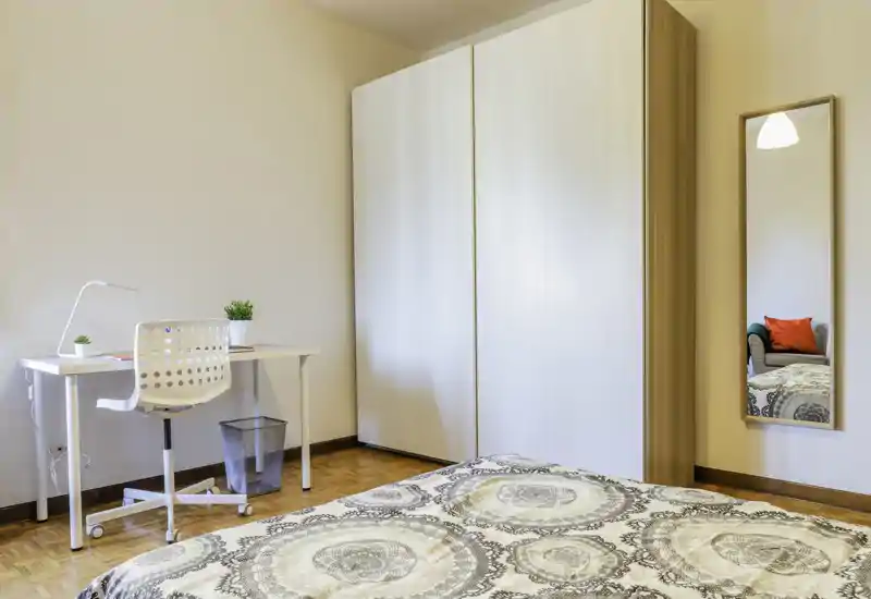 Dormitorio luminoso y bien decorado con ropa de cama estampada, un gran armario blanco, un escritorio pequeño y silla; ideal para una persona que busca un espacio moderno y ordenado.