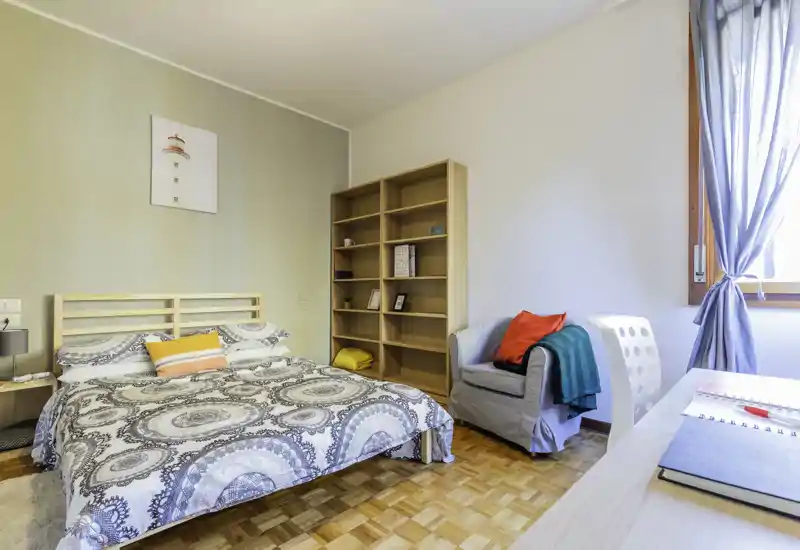 Dormitorio luminoso y bien presentado con cama doble, textiles acogedores y un sillón junto a la ventana. La luz natural y la decoración neutra crean un ambiente agradable, perfecto para anuncios de alquiler.