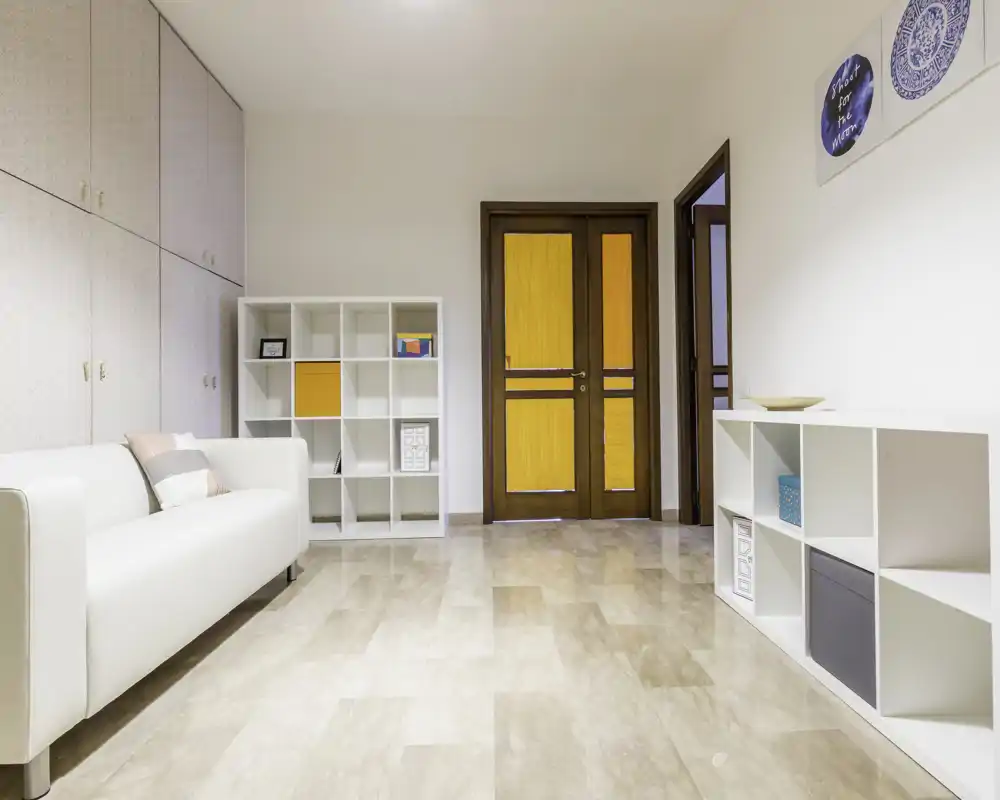 Sala luminosa y minimalista con un sofá blanco, estanterías modulares y puertas de madera cálida — líneas limpias y tonos neutros que crean un espacio acogedor.