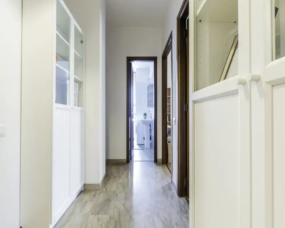 Pasillo/entrada bien iluminado con suelo pulido, armarios blancos y puertas que conducen a otras habitaciones — zona de acceso clara, limpia y acogedora.