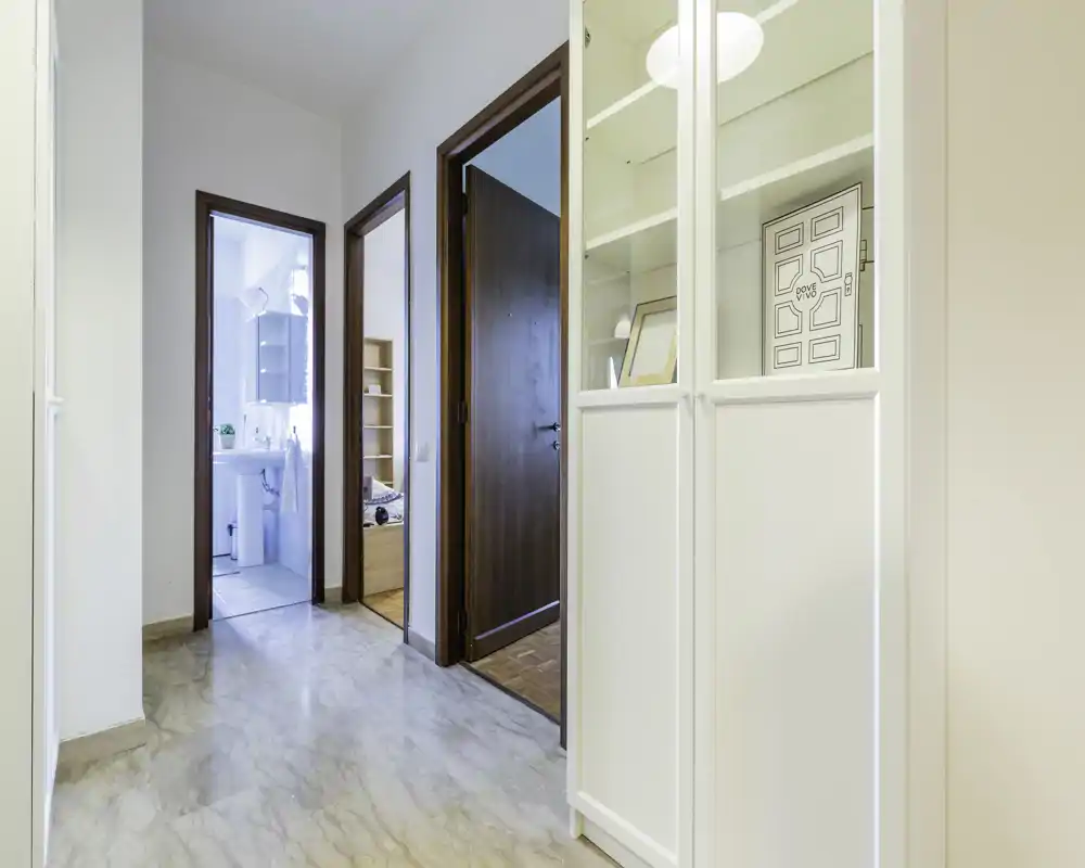 Entrada luminosa y limpia con suelo efecto mármol, armario empotrado y puertas que conducen al baño y al dormitorio.