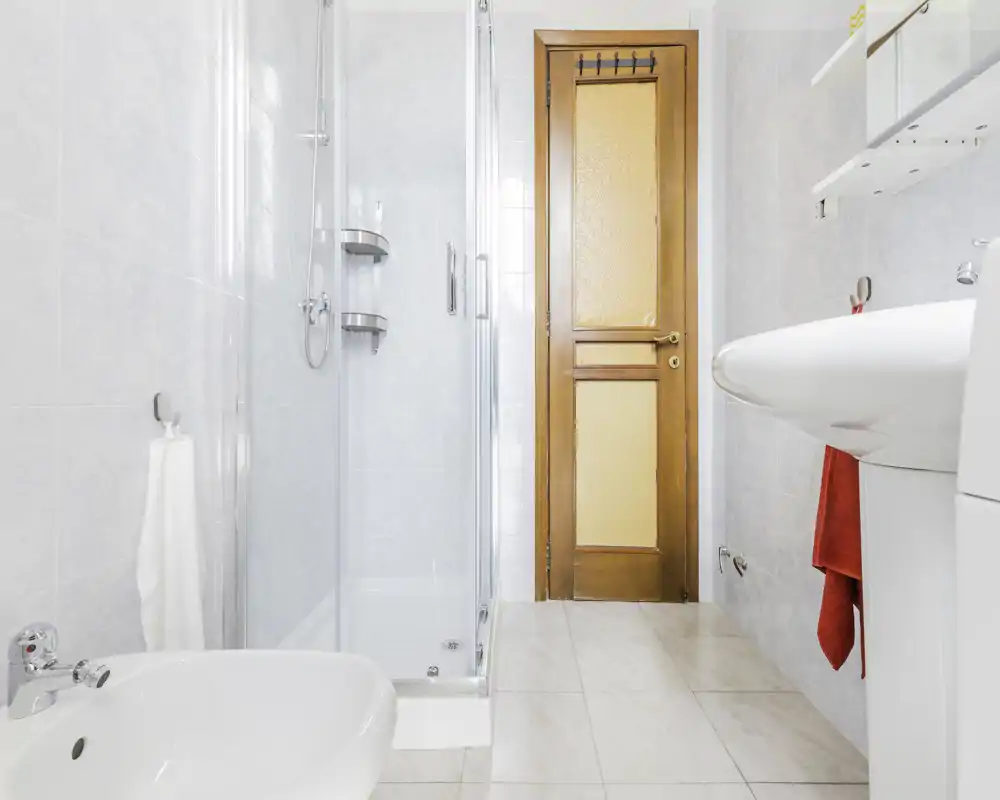 Bagno luminoso e pulito con box doccia in vetro, bidet, lavabo e pavimento piastrellato — ideale per affitti brevi che cercano un bagno ben curato.