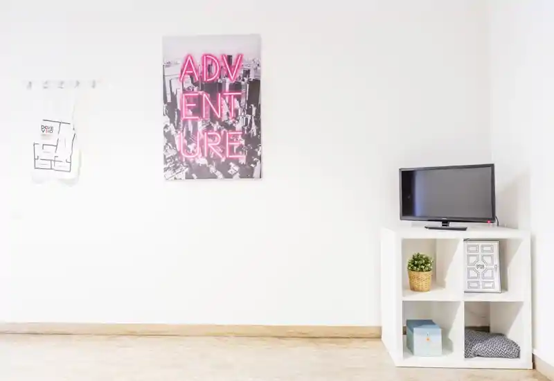 Bright, minimalist living area with white walls, small media cabinet and decorative wall art. The room feels airy and uncluttered, ideal for a compact rental living space.