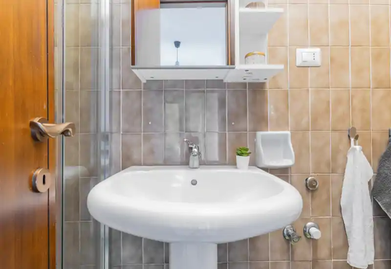 Clean, well-lit bathroom sink area with a pedestal basin, wall tiles, mirror cabinet and small accessories.