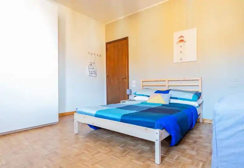 Chambre lumineuse au style épuré avec un lit double en bois habillé d'une couette bleue géométrique, sol en parquet et décoration minimale avec table de chevet et lampe.
