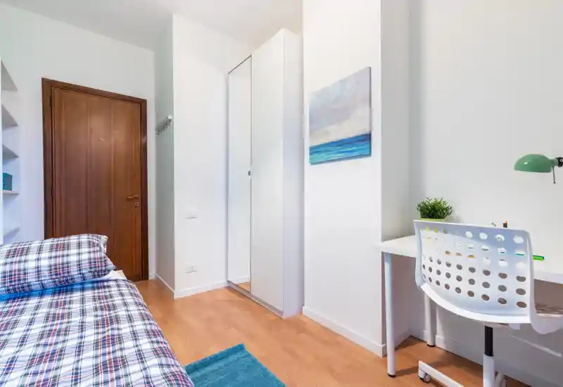 Bright, modern single bedroom with a neatly made bed, white wardrobe with mirror, and a compact study desk — ideal for a student or professional.