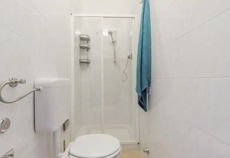 Compact, clean bathroom with a shower cabin, wall-mounted cistern and a towel hanging on the wall. Bright, neutral tiles create a neat and practical space ideal for short stays.