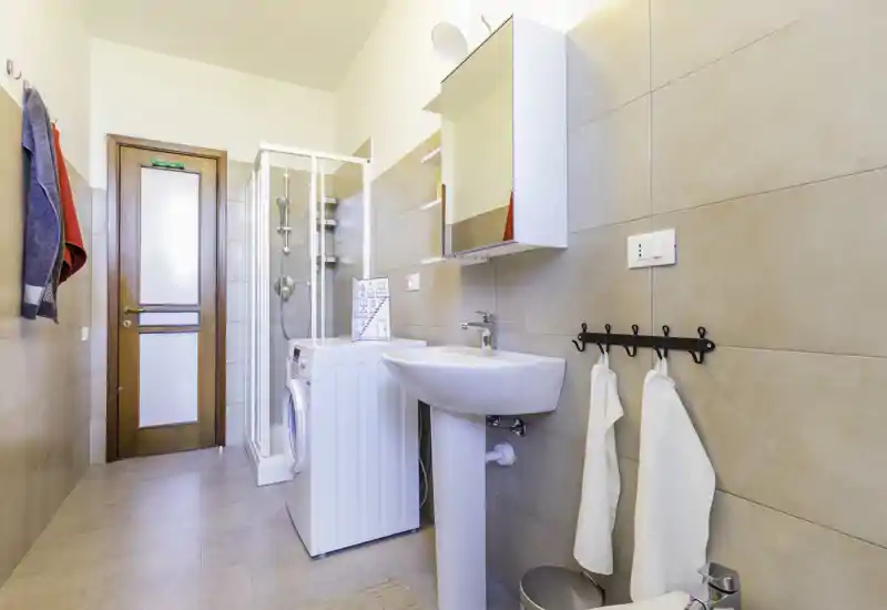 Bright, modern bathroom with a pedestal sink, wall-mounted mirror cabinet, shower enclosure and a washing machine — clean, well-lit and practical.