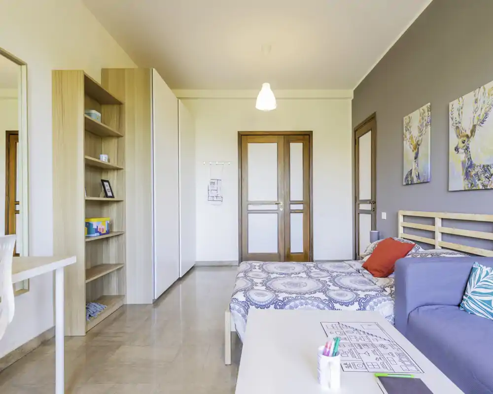 Camera da letto moderna e luminosa con letto matrimoniale decorato, cuscini accoglienti e semplici scaffali — perfetta per soggiorni brevi o lunghi.
