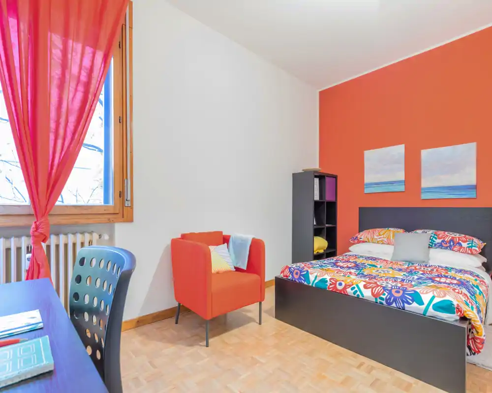 Bright, colorful bedroom with a double bed dressed in vibrant floral bedding, an accent armchair and a desk by the window — ideal for a cheerful rental listing.