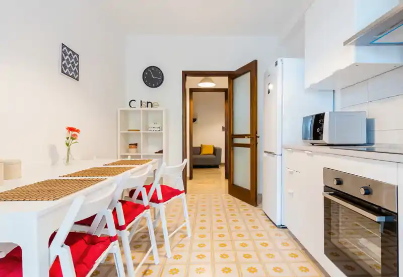 Bright, modern kitchen with white cabinets, built-in oven, microwave and a dining table with red-cushioned chairs; patterned floor tiles add character.