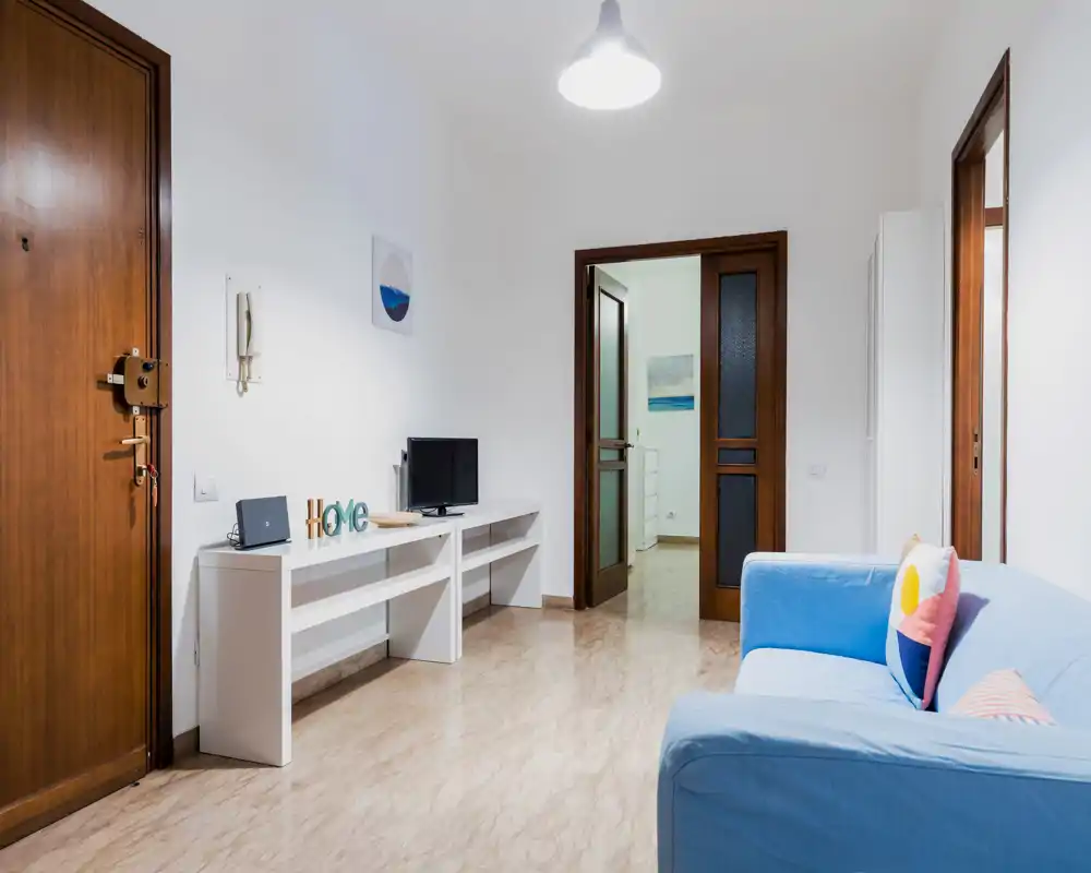 Soggiorno luminoso e moderno con divano blu, consolle semplice con TV e elementi decorativi — design pulito e minimale, ideale per affitti brevi.