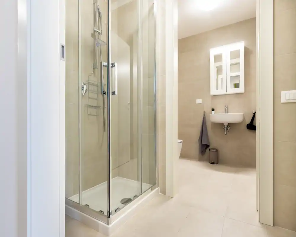 Modern, clean bathroom with a glass shower cubicle, wall-mounted sink and neutral beige tiles. Bright, minimal and well-maintained space ideal for rental photos.