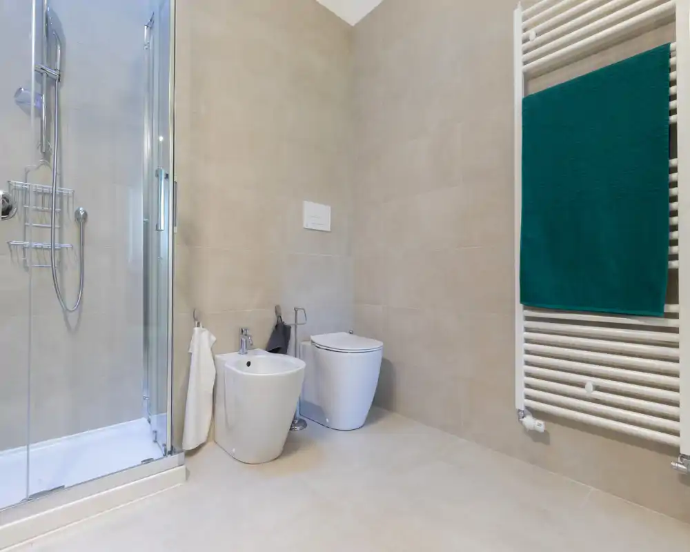 Modern, well-lit bathroom with shower enclosure, bidet, toilet and towel radiator. Neutral tiles and clean lines create a fresh, minimal look.