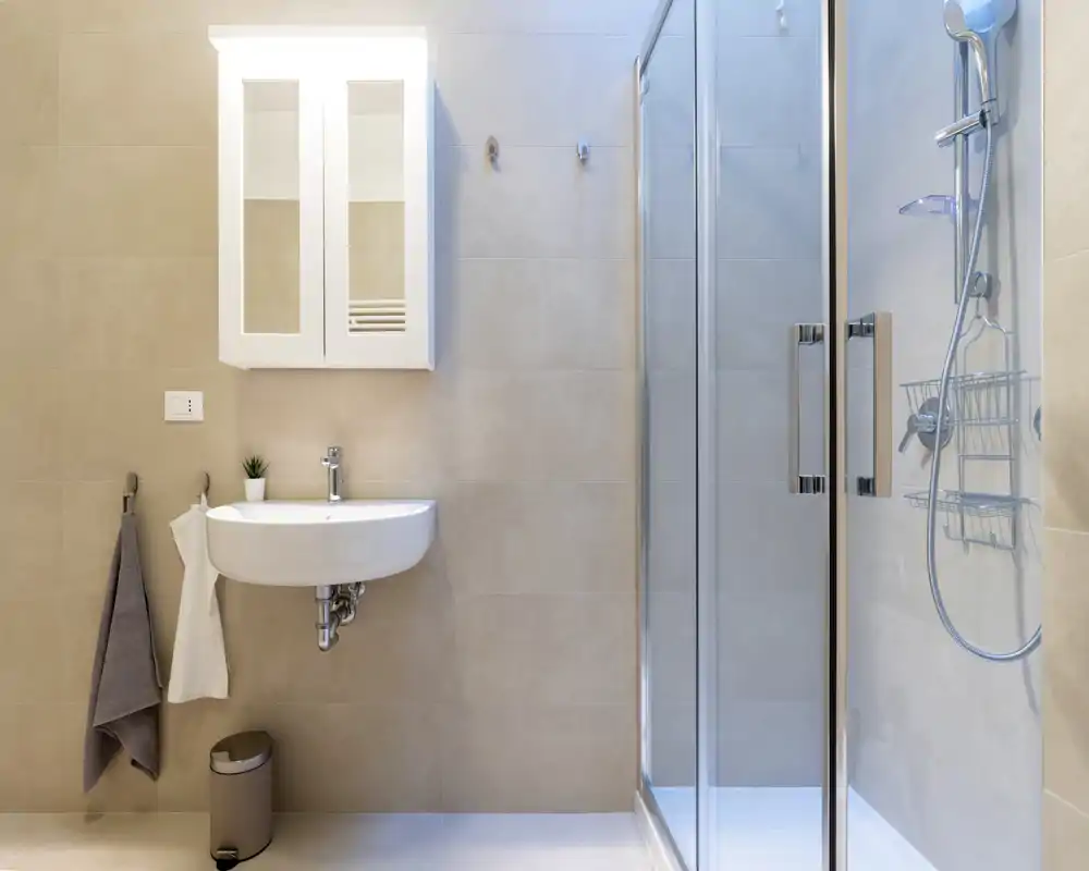 Modern, well-lit bathroom with a glass-enclosed shower, wall-mounted sink, mirrored cabinet and neutral tile walls.