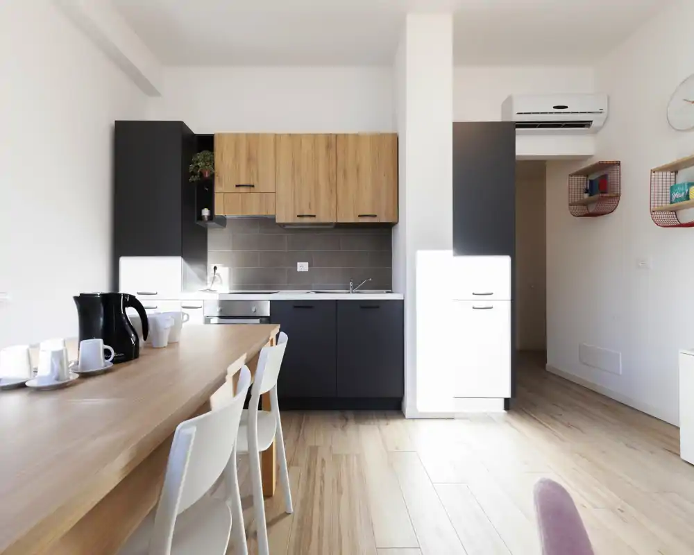 Modern compact kitchen with dark lower cabinets and warm wood upper cabinets, integrated appliances and a wooden dining counter with seating — bright and neatly styled for rental photos.