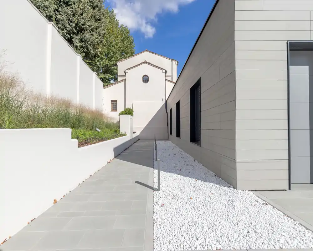 Modern outdoor walkway beside a contemporary building, featuring clean paving, white decorative gravel and a low retaining wall under bright daylight.