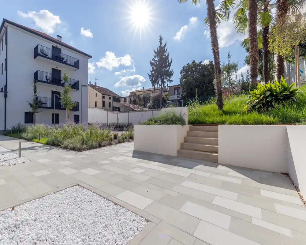 Sunny landscaped courtyard with paved walkways, planted beds and terraced greenery — ideal for relaxing outdoors.